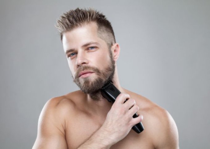 Mężczyzna trymuje brodę przy pomocy maszynki do włosów i brody